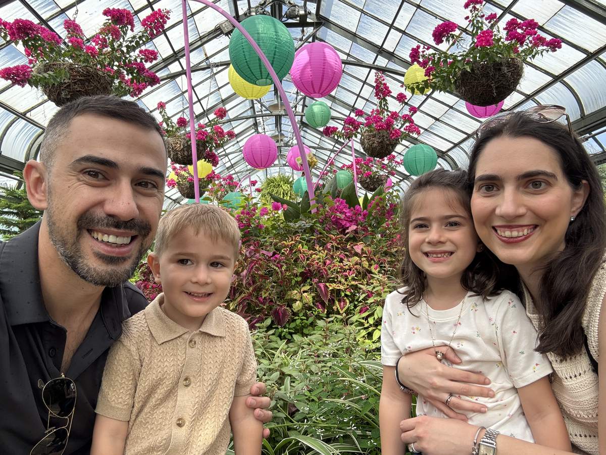 Nick and his family smiling together in a greenhouse full of flowers and paper lanterns.